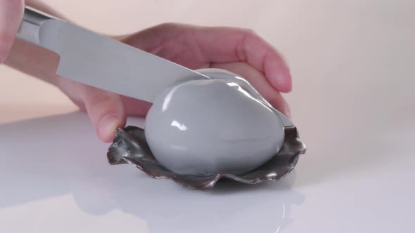 Pastry Chef Cuts Dessert in the Form of Pearl with Gray Glaze on White Background