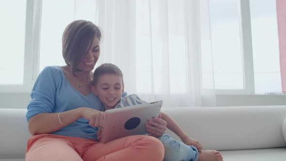 Mother and Son Sitting on Sofa Using Digital Tablet