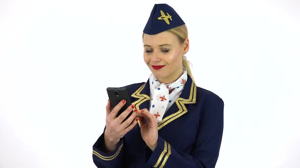 A Young Beautiful Stewardess Works on a Smartphone with a Smile - White Screen Studio