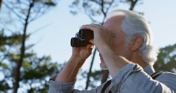 Senior man looking through binoculars at countryside