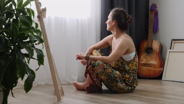Woman artist painting on canvas using acrylic paints sitting on the floor at home