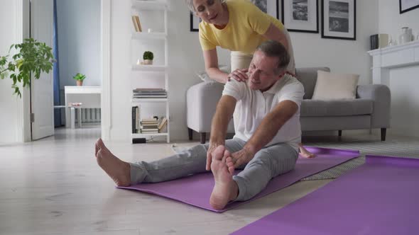 Fit Active Mature Wife Helping Senior Husband Doing Stretching Exercise at Home