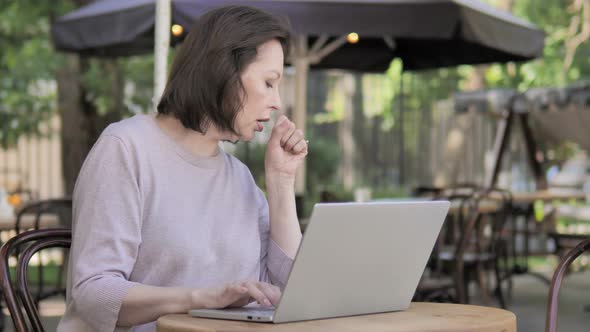 Coughing Old Woman Working on Laptop in Outdoor Cafe
