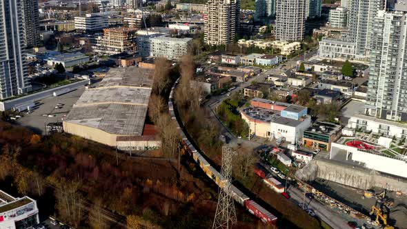 Container Train Passing Though Burnaby City With High-rise Buildings In Canada. - aerial tilt up