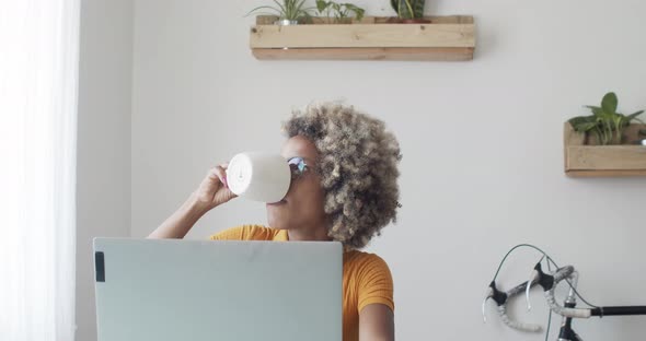 African American Woman Drinking Coffee While Working at Home or in an Office with a Laptop