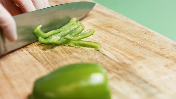 Top view on dark-skinned man hands by knife cut on slices big green bell pepper