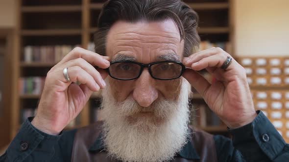 Bearded Man with Wrinkled Face Putting on His Eyeglasses and Posing on Camera