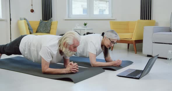 Senior Couple Doing Elbow Plank at Home and Simultaneously Revisioning Video Lessons