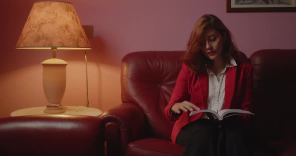 Young Italian girl sitting with red jacket reads book on the sofa