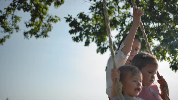 Mother Shaking Two Small Sisters on a Swing with Rope Handles