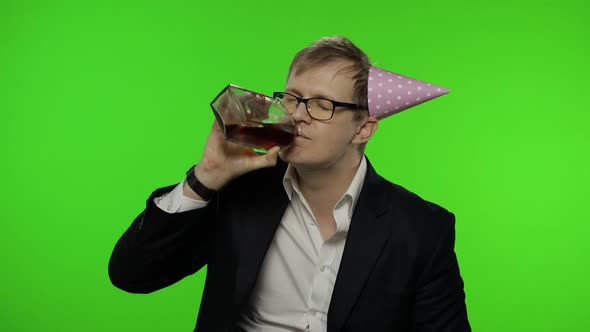 Drunk Sleepy Young Businessman with Hangover in Festive Cap Drinks Alcohol