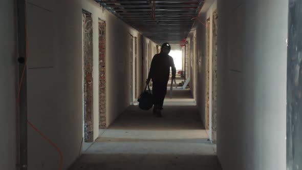 Silhouette of a Construction Worker Walking Down a Dark Corridor with a Tool in His Hands