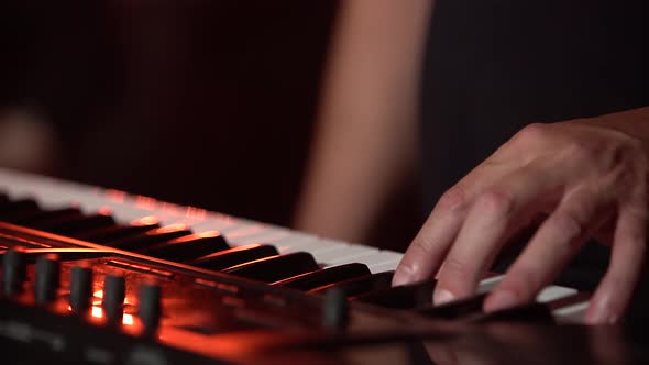 Male Hands Playing on Synthesizer Piano Keyboard in Dark Studio with Neon Lighting. Dynamic Neon