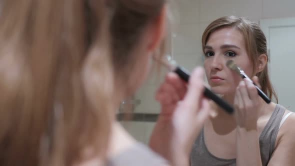 Young Woman Putting Make Up on Face in Mirror