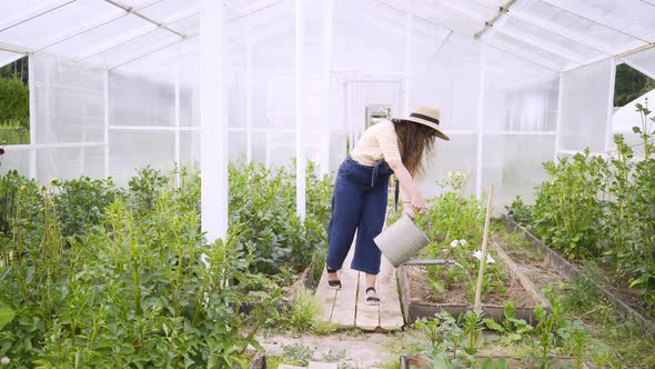 Girl with Can Walks on Path To Water Flowers in Greenhouse