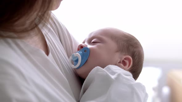 Little Newborn Baby Boy Sleeping with Baby Dummy on Mother Hands at Home Mom Puts Baby to Sleep