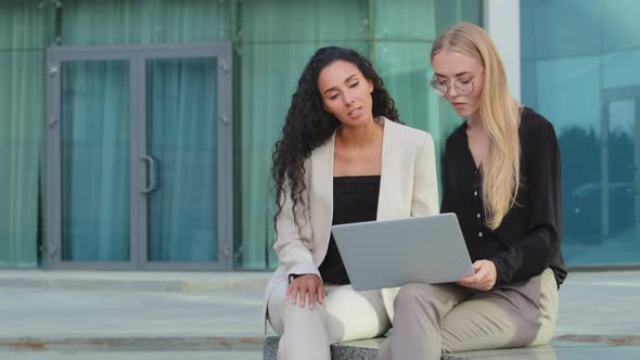 Two Diverse Businesspeople Chatting Sitting Behind Laptop Outdoors