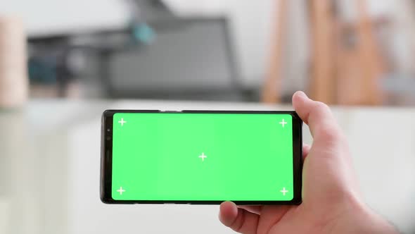 Man Holding Horizontally a Smartphone with Green Screen on