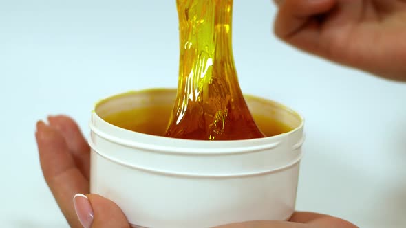 Beautician removes sugar paste from a white jar with a wooden spatula before the sugaring procedure