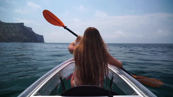 Young Attractive Brunette Woman with Long Hair in White Swimsuit Swimming on Transparent Kayak