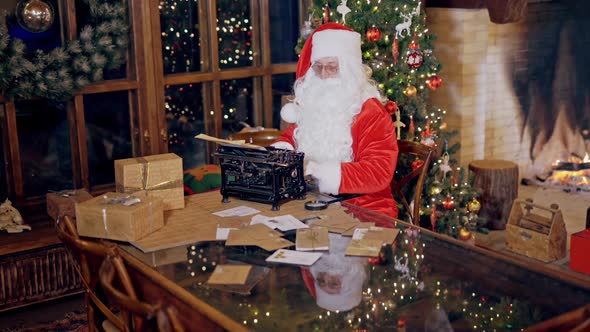 Santa Claus typing holiday letters in his residence. Christmas decorations, presents
