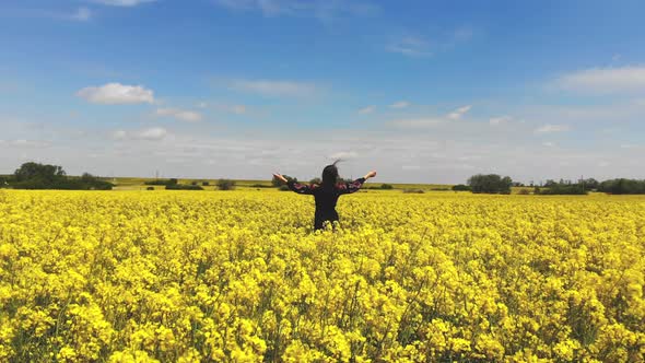 Aerial View Woman Stands with Her Back To the Camera with Her Hands Raised To the Sky in a Field