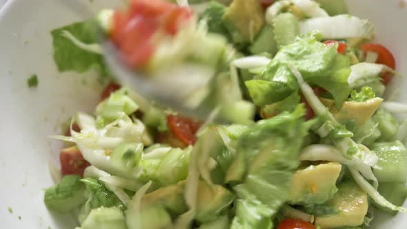 Woman Mixes Delicious Fresh Salad with Spoon in White Bowl