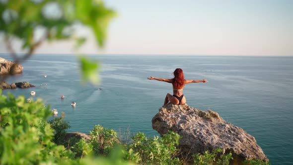 Woman in Swimsuit Sit on Rock Raises Her Hands Up Feeling Happiness Backdrop Sea