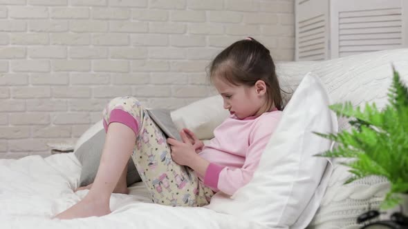 Cute Little Child Girl Lies in Bed Uses Digital Tablet