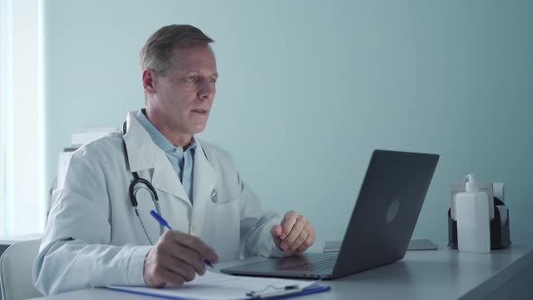 Senior Old Male Doctor Consulting Patient Online By Video Call on Laptop