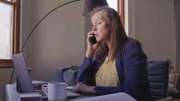 Woman talking on smartphone while using laptop at home