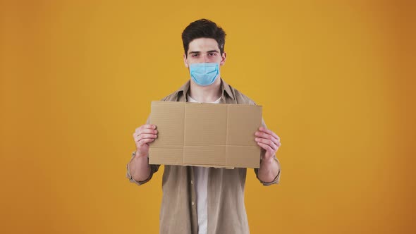 Young Guy in Protective Mask is Looking Serious Showing an Empty Cardboard Tablet While Posing on