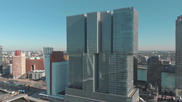 Aerial, slow pan drone footage of a skyscraper along the shore of a water channel of Rotterdam