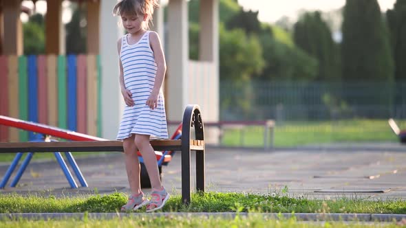Cute Child Girl Waiting for Her Mother Sitting on a Bench on Summer Playground in Kindergarten Yard
