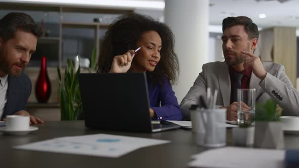 Multiracial Coworkers Talking Finance Using Laptop in Modern Company Office