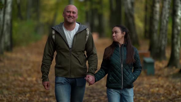 Amorous Smiling Couple Middle-aged Woman with Dark Hair and Bald Man Walking Through the Autumn