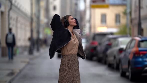 Young Woman Listening To Music with Headphones Outdoors. She Walks Through the Autumn Crowded City