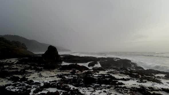 Gliding across wave battered rocky Oregon coast, storm clouds on the horizon, aerial