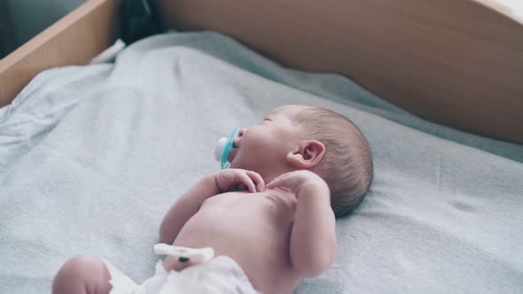 Newborn Baby with Short Blond Hair and Pacifier in Mouth