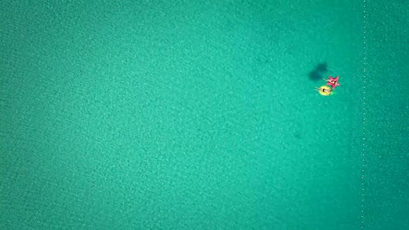 Aerial view of man and woman floating by string buoy on inflatable mattresses.