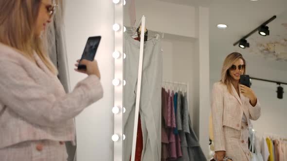 Cheerful Woman Taking Pictures Near Mirror in Shop