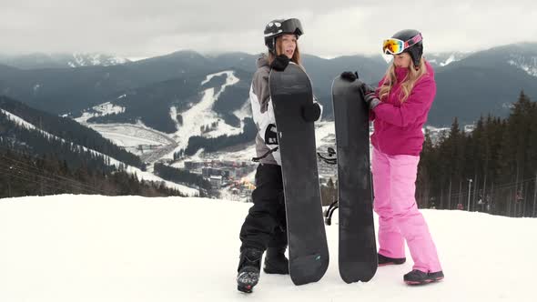 Two Stylish Women with Their Snowboards on Mountain