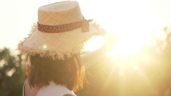 Back View of Charming Caucasian Woman in Straw Hat Stretching Hand to Sunshine Turning to Camera in