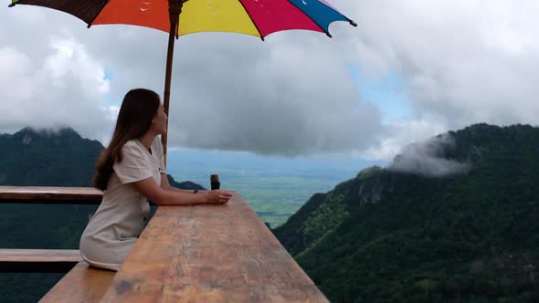 A female traveler sitting on a wooden balcony and looking at a beautiful mountain and nature view