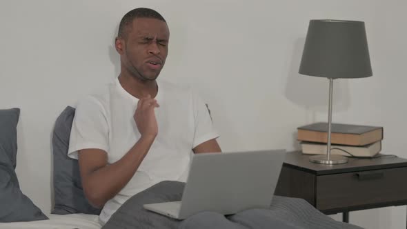 African Man with Laptop Having Neck Pain in Bed