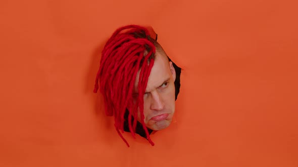 Young Man with Sad Expression on His Face Sticking Out of Hole of Orange Background