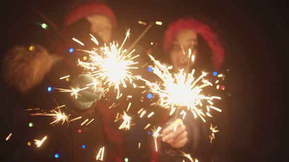 Two Young Smiling Women Friends Playing with Sparklers at Night and Dancing - Looking in the Camera