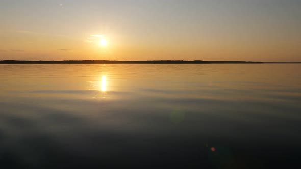 Smooth lake water, sunset hour, bright sun shine low, dark stripe of land