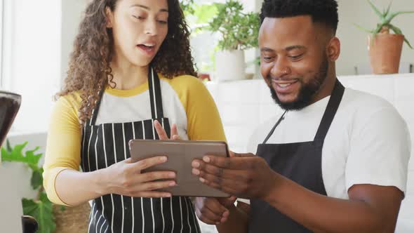 Happy african american male cafe owner and biracial female barista using tablet at cafe