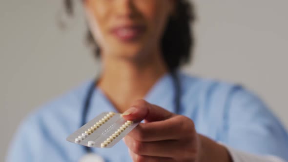 Video of smiling biracial female doctor with pills on blue background